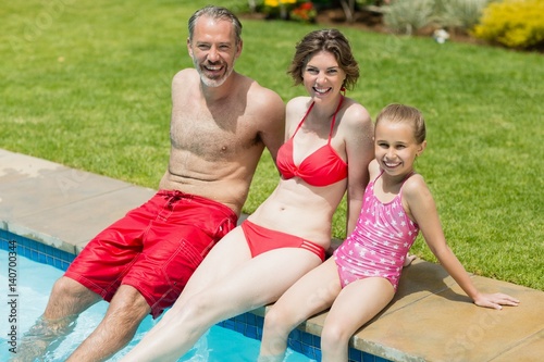 parents and daughter sitting on poolside 