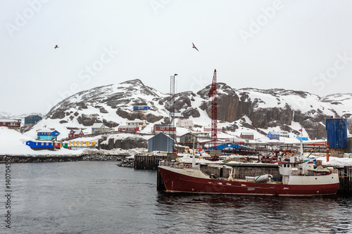 Fishing boat at the pier of Maniitsoq village with colorful houses on the rocks in background, Greenland photo