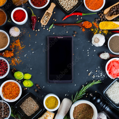 Large set of spices, herbs, vegetables and smartphone on black background