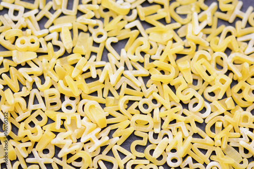 Uncooked alphabet or letter-shaped pasta spread on a black background