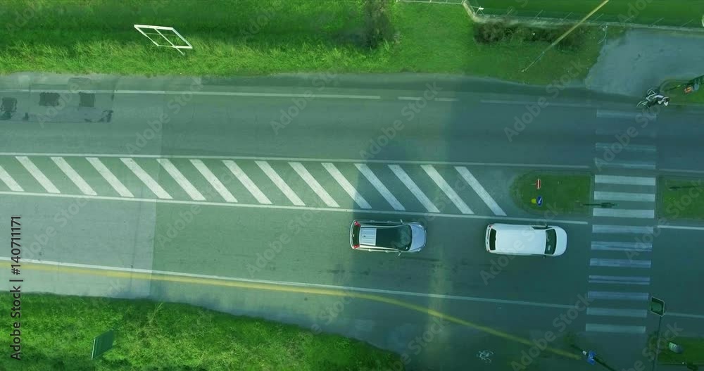 Cars on the road stopped for a red light, skipping the bicyclist. A cyclist crosses the roadway through a pedestrian crossing aerial shot top view Cars on the road stopped for a red light, skipping the bicyclist. A cyclist crosses the roadway through a pedestrian crossing aerial shot top view