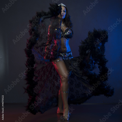 Fototapeta Naklejka Na Ścianę i Meble -  Sexy slim woman, belly dancer in black costume with crystals. Dark background with pink and blue lightening
