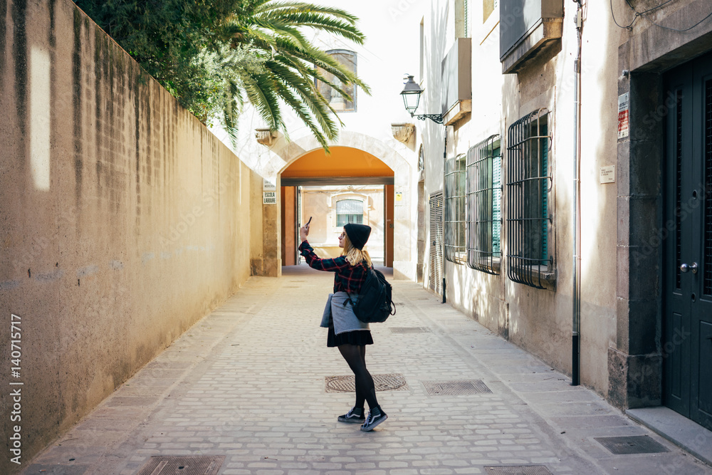 Young hipster woman making photo of palm tree in alleyway nice light and flannel shirt with beanie Young hipster woman making photo of palm tree in alleyway nice light and flannel shirt with beanie