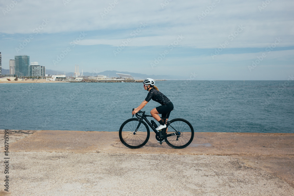 Female professional cyclist spins on pier in nice light by the seaside