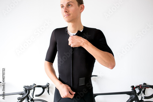 Professional cyclist preparing for a bike ride all white room all black outfit zipping jersey with bikes in back photo