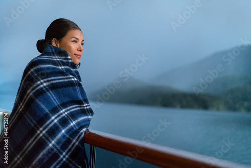 Cruise ship passenger on Alaska travel vacation enjoying scenery at dusk on suite balcony deck with wool throw in cold weather. Asian tourist woman relaxing on summer holiday cruising adventure. © Maridav