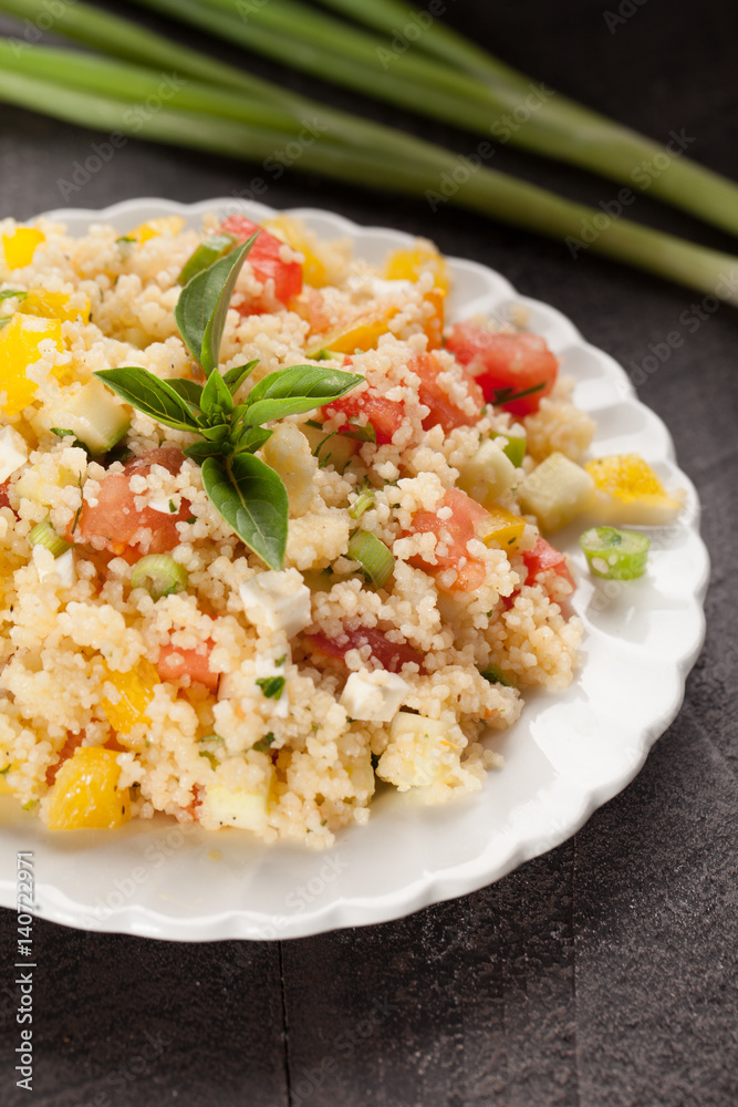 Tabbouleh salad with couscous, tomatoes, onion, zucchini and bell peppers topped with basil leaf close up shot