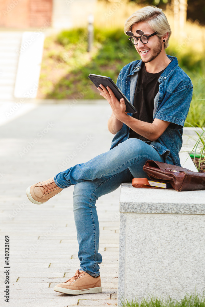 Obraz premium Hipster smiling guy with tablet sitting on ledge