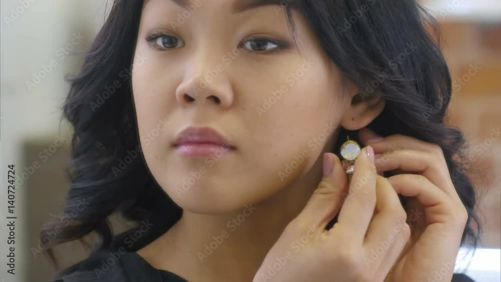 Young asian woman puts on beautiful earrings Young asian woman puts on beautiful earrings