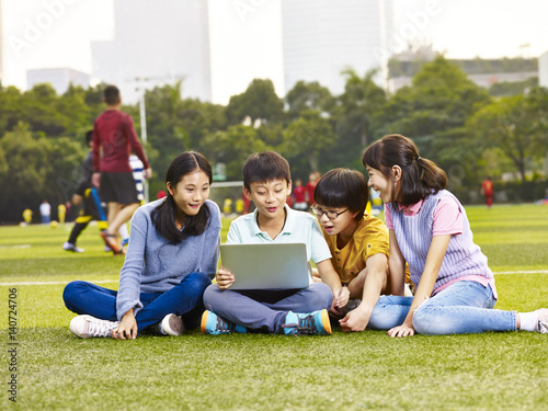 Photography asian elementary school boys and girls sitting on playground grass using laptop