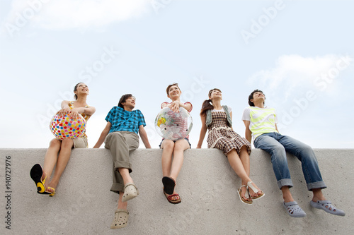 Five young people sitting on breakwater, women holding beach balls photo