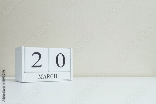 Closeup white wooden calendar with black 20 march word on blurred white wood desk and cream color wallpaper in room textured background with copy space , selective focus at the calendar