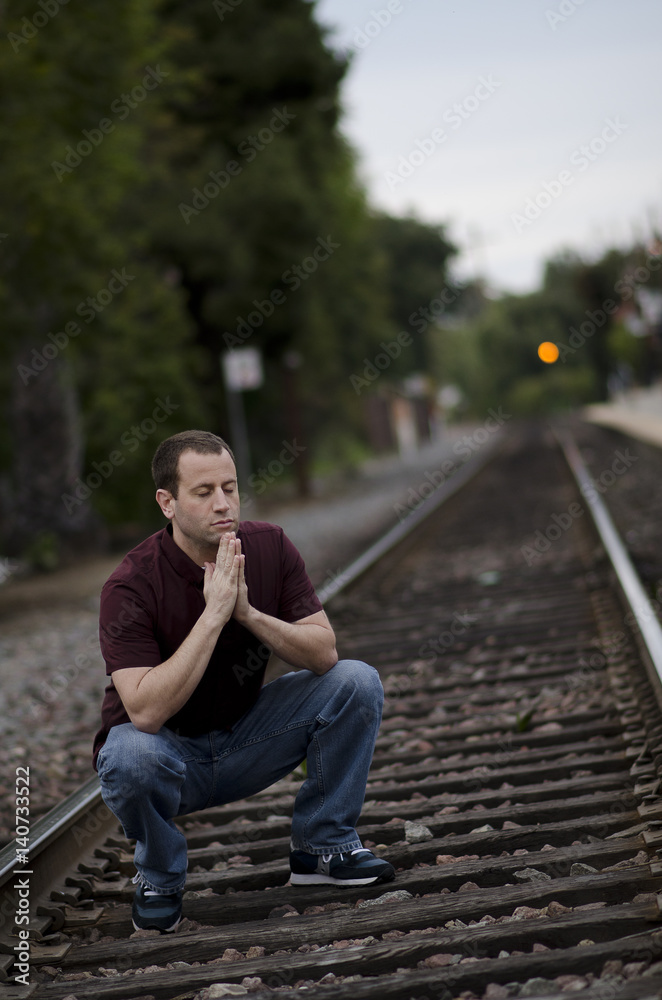 Man crouching to pray on rail road tracks. Man crouching to pray on rail road tracks.