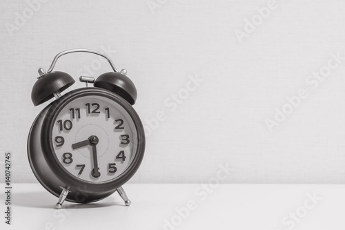 Closeup alarm clock for decorate show half past eight or 8:30 a.m.on white wood desk and cream wallpaper textured background in black and white tone with copy space