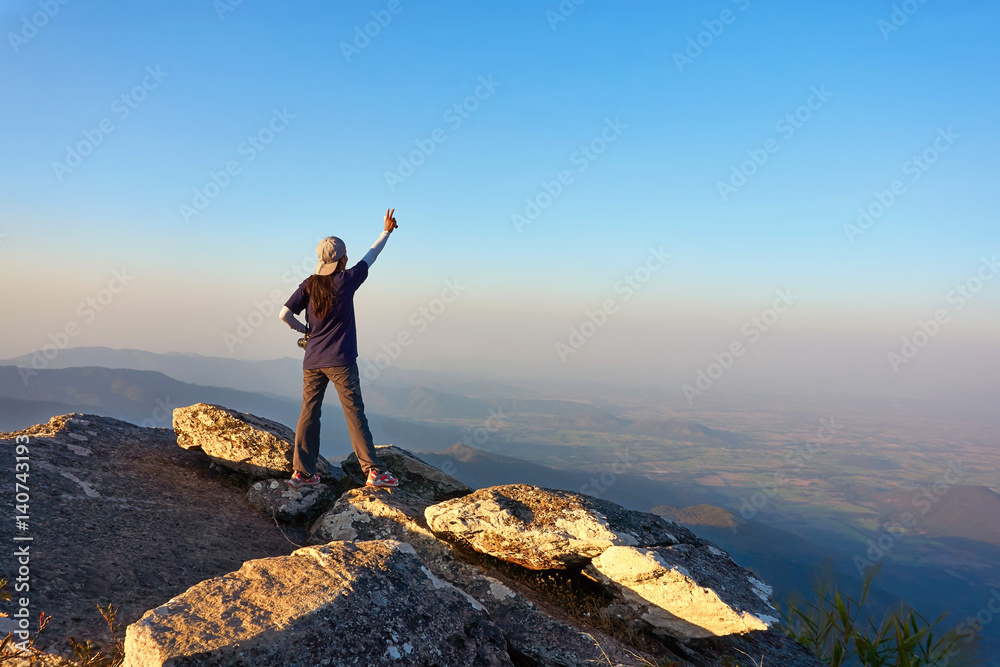 Young traveler is standing at the mountain view point, rises her hand up under the beautiful clear sky. Young traveler is standing at the mountain view point, rises her hand up under the beautiful clear sky.