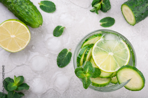 Refreshing water with cucumber, mint and lime on grey background top view. Summer drink cucumber lemonade. Healthy drink and detox concept
