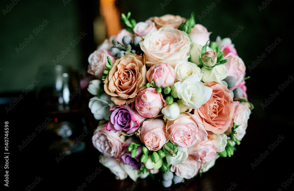 Gorgeous wedding bouquet made of tender pink and orange roses lies on table