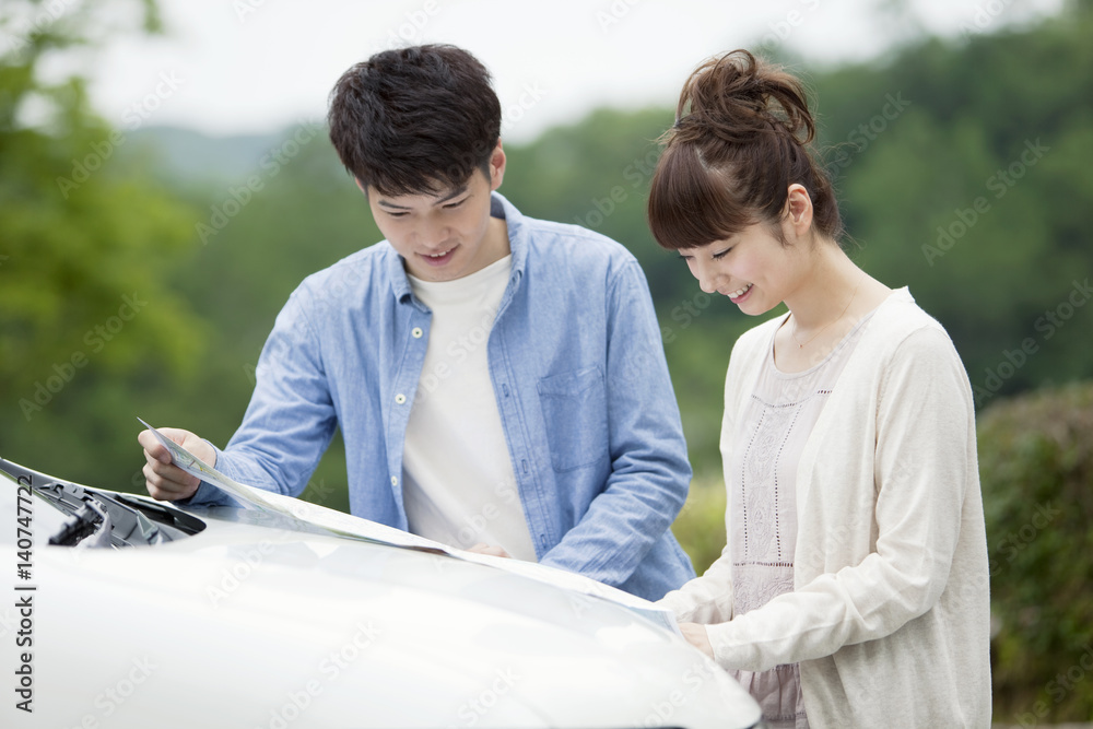 © amanaimages - Couple looking at a map in front of a car