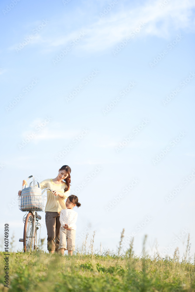 Girl with mother walking at riverbank, mother pushing bicycle, copy space Girl with mother walking at riverbank, mother pushing bicycle, copy space
