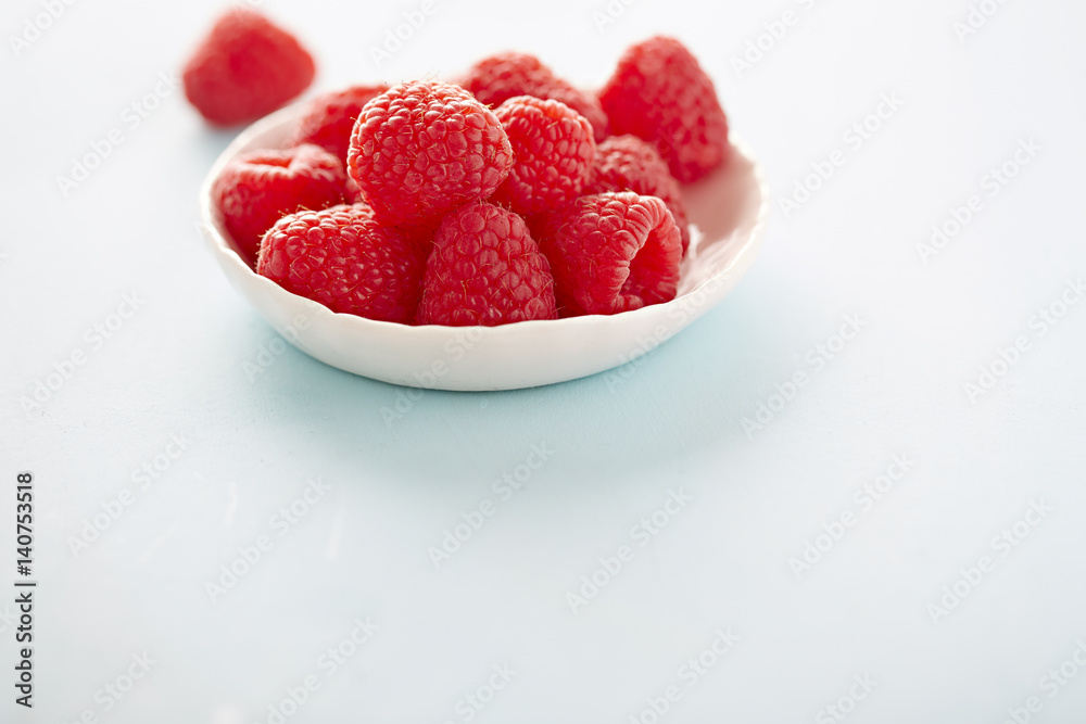 Raspberries in white bowl and blue background Raspberries in white bowl and blue background