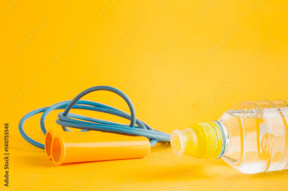 Water bottle and skipping rope on a yellow background