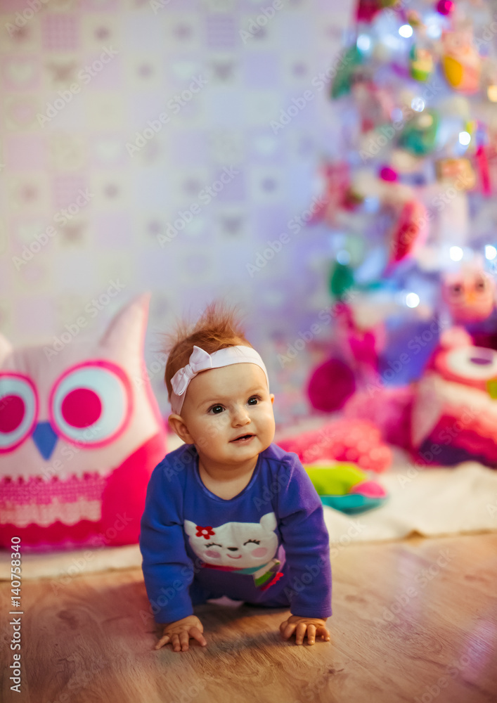 Little girl in blue baby-suit sits on wooden floor before toy Christmas tree Little girl in blue baby-suit sits on wooden floor before toy Christmas tree