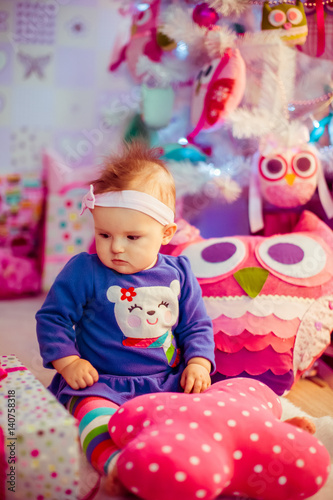Busy little child in blue dress sits among pink toys on the floor