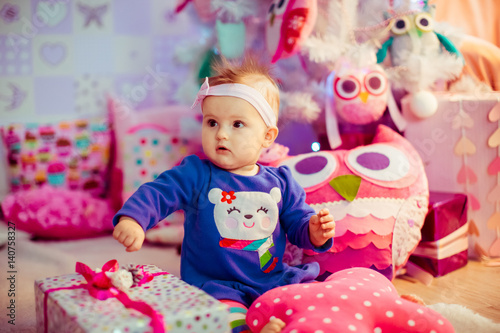 Little girl in blue dress with bear sits among soft pink toys on the floor © pyrozenko13