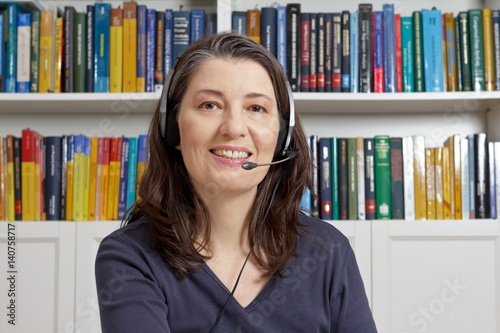 Friendly smiling woman with head set during the live streaming of an english lesson, telelearning, e-education.