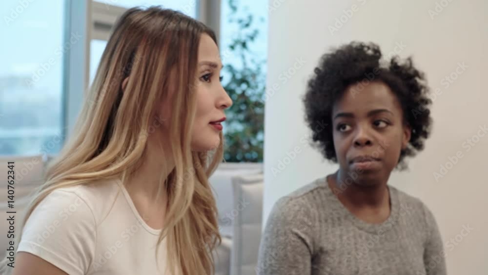 PAN of Caucasian and African women sitting beside female Asian colleague and listening to her telling funny story PAN of Caucasian and African women sitting beside female Asian colleague and listening to her telling funny story