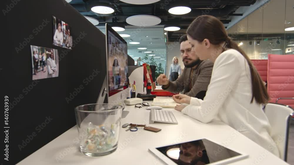 PAN of team of businesspeople working in office: businesswoman and businessman looking at notebook; group of coworkers discussing problem with frustrated male colleague working on computer