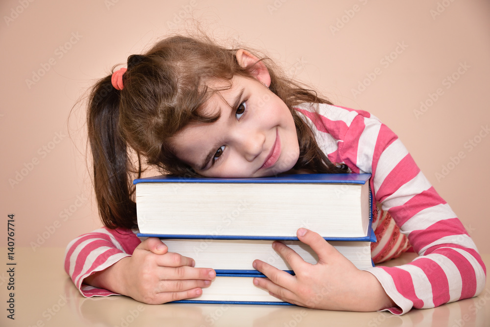 Smiling young girl sitting at the table with her head on the books Smiling young girl sitting at the table with her head on the books