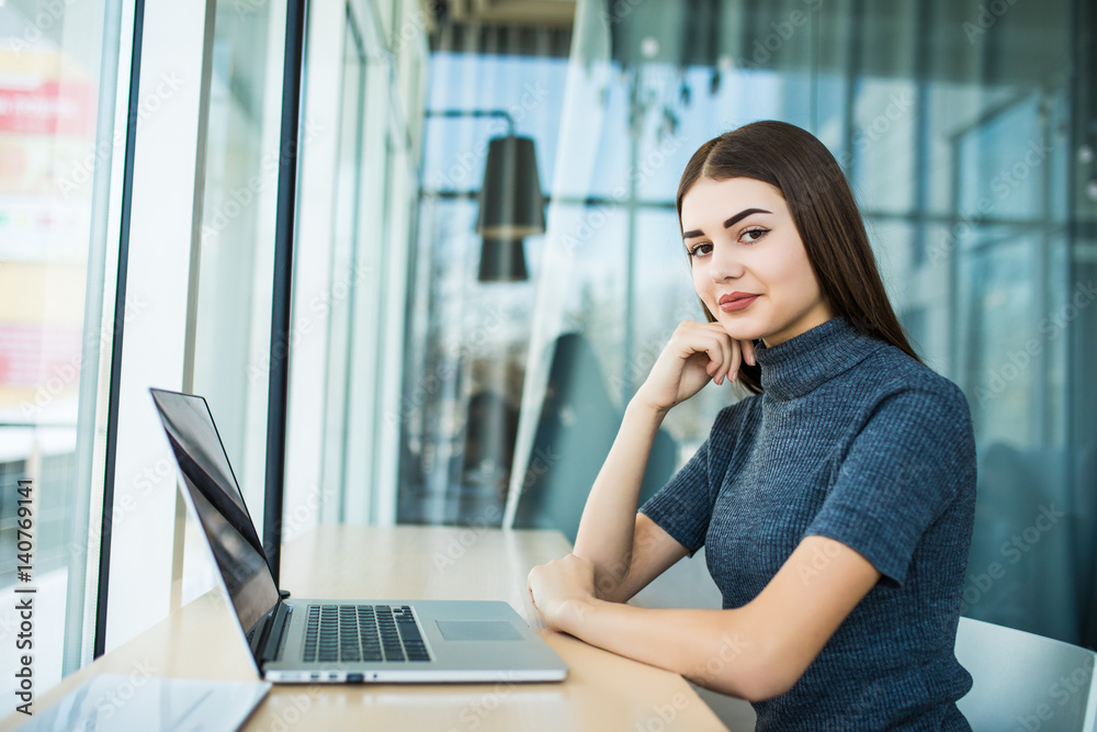 Side view of brunette woman using laptop computer sitting against big window in office Side view of brunette woman using laptop computer sitting against big window in office