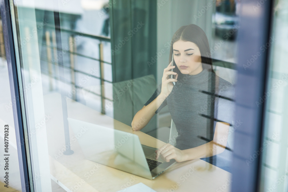 Young woman talking on phone and using tablet computer through the window Young woman talking on phone and using tablet computer through the window