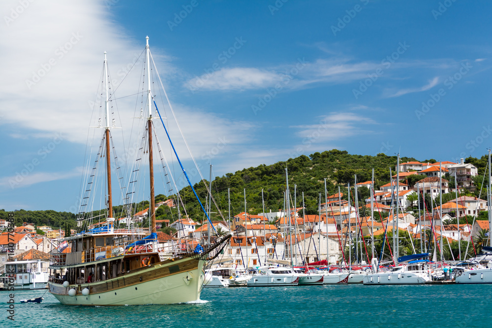 Ship sails in the sea bay of croatian city Sibenic on bright sunny day. Harbor, yachts and red roofs of the town on background.