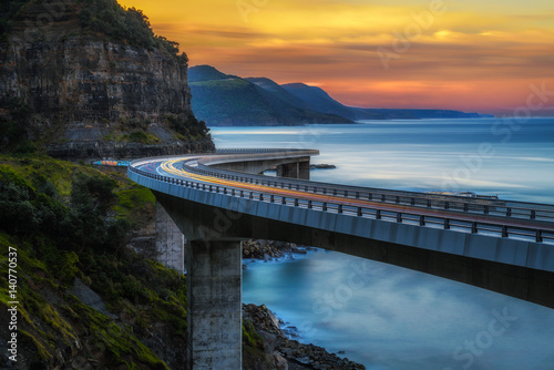 Sunset over the Sea cliff bridge along Australian Pacific ocean coast with lights of passing cars
