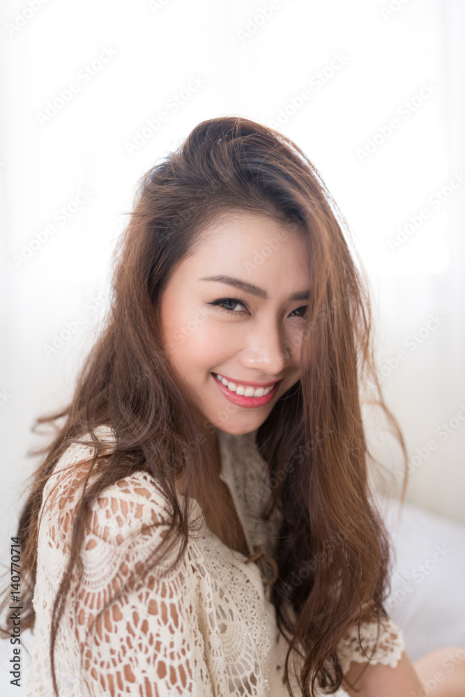 Asian woman breathing and sitting on a bed at home with a window in the background Asian woman breathing and sitting on a bed at home with a window in the background