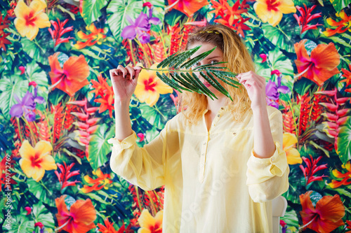 Portrait of a woman hiding behind palm branch on bright colorful background