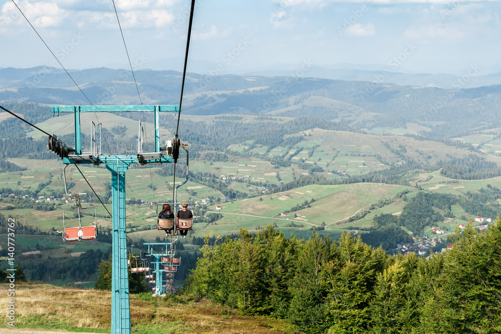 Young couple going down on ski lift, Carpathian mountains background.