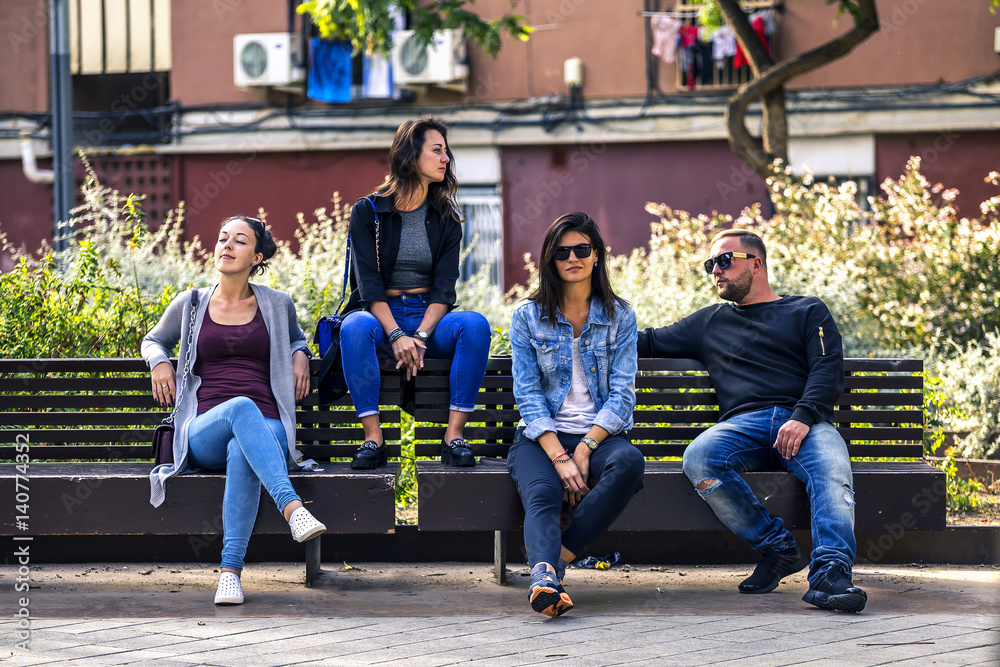 Fototapeta premium Young and attractive people are sitting on a bench in ghetto street, enjoying the sunny day. Barcelona, Spain