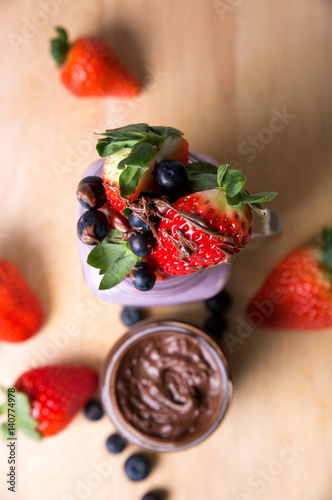 fruits strawberries and blueberries with chocolate topping in a glas wooden background