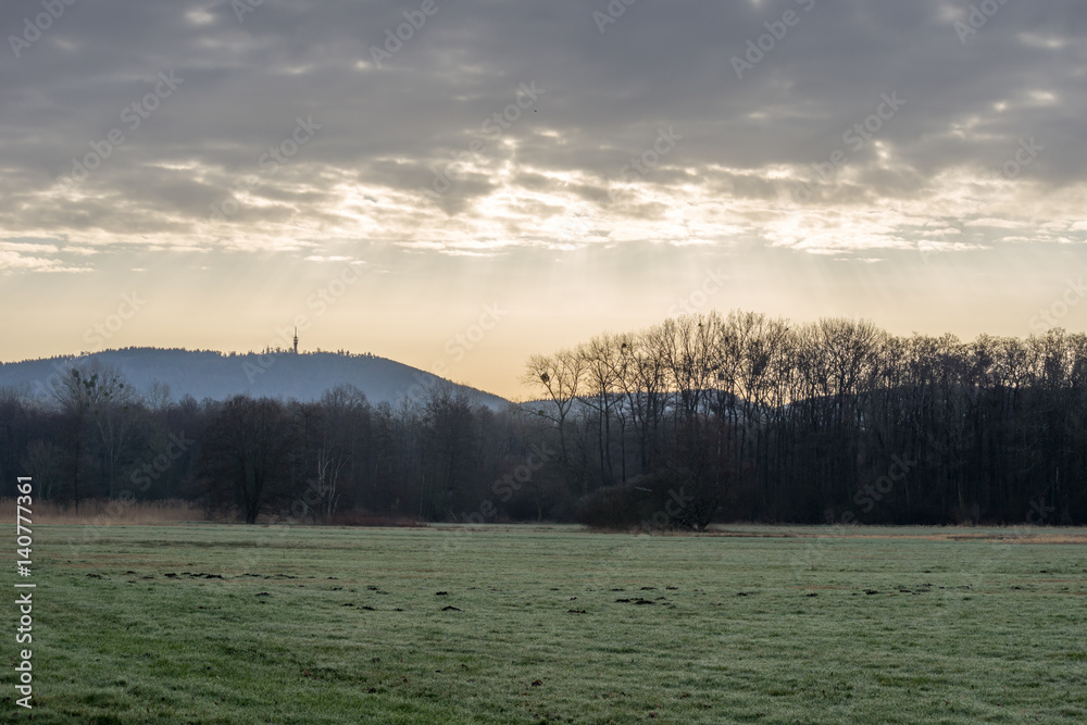 Fototapeta premium Meadow and forest with mountain Fremersberg in the background and sky with sunbeams