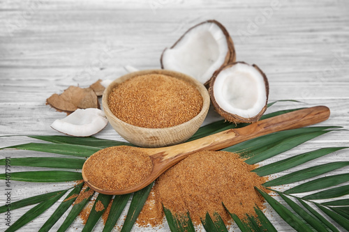 Bowl and spoon of brown sugar with coconut on wooden background