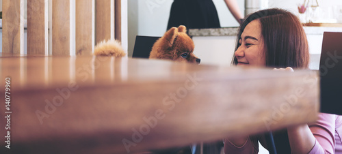 A happy Asian woman looking and playing with pomeranian dog in cafe photo