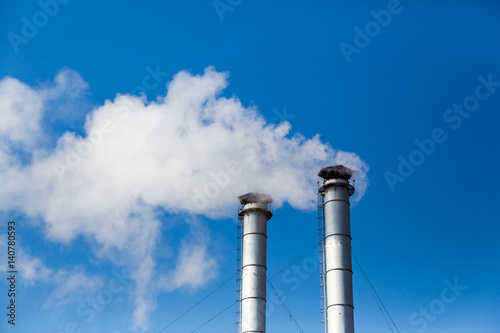 The smoke from the chimneys of a heating plant in the background of blue sky. Pollution of the environment. The exhaust emissions from the chimneys into the atmosphere