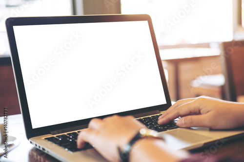 Mockup image of hands using laptop with blank white screen on vintage wooden table in loft cafe