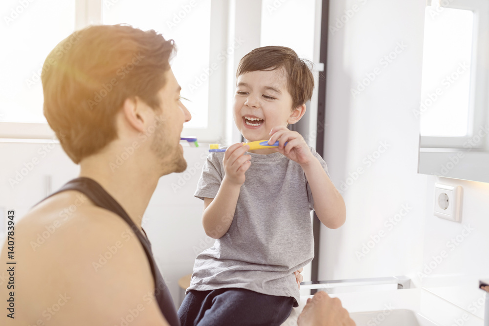 Happy father and son brushing teeth together in bathroom Happy father and son brushing teeth together in bathroom