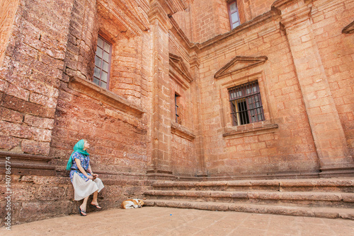 Beautiful woman relaxing on stone stairs of historical cathedral of Goa, built in 17th century