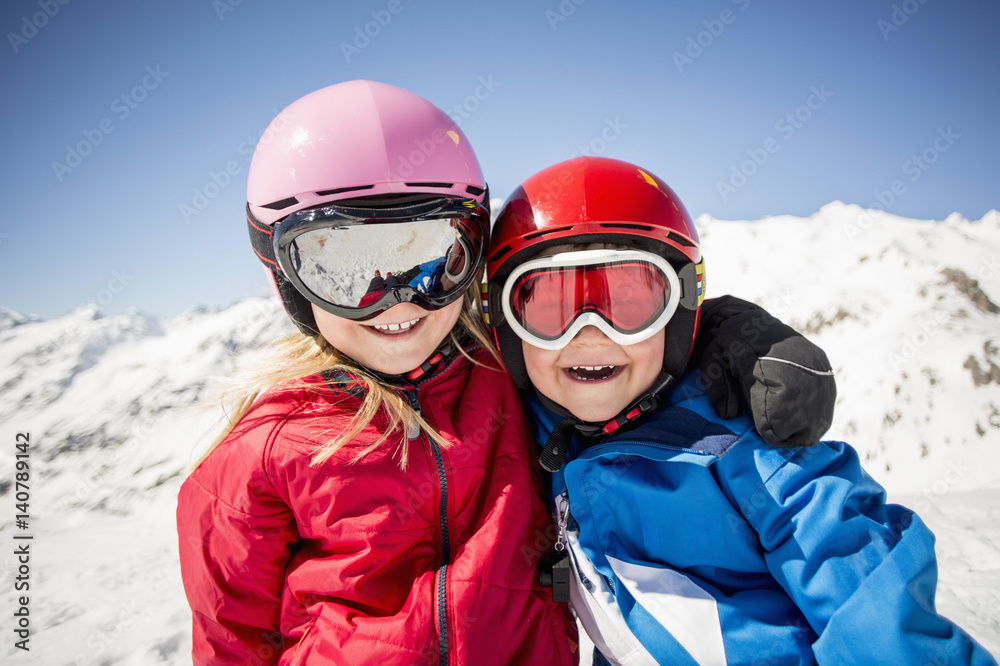 Cheerful siblings in ski-wear standing against snowcapped mountain
