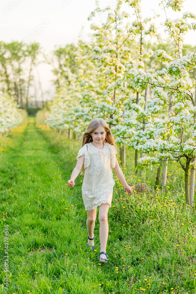 A beautiful little girl runs through a flowering garden in the spring A beautiful little girl runs through a flowering garden in the spring